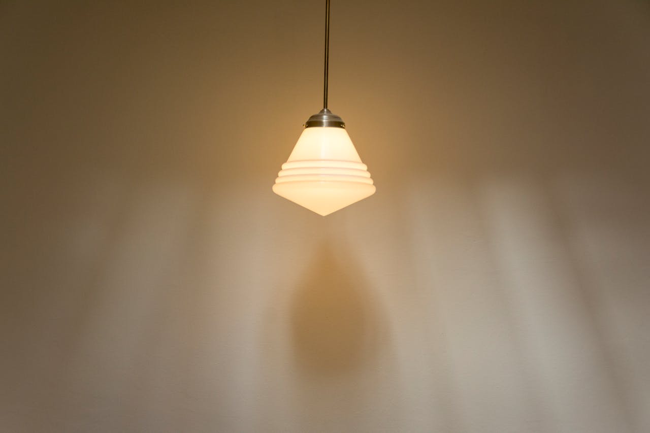 A simple hanging lamp casting soft light and shadows on a wall, emphasizing minimalism.